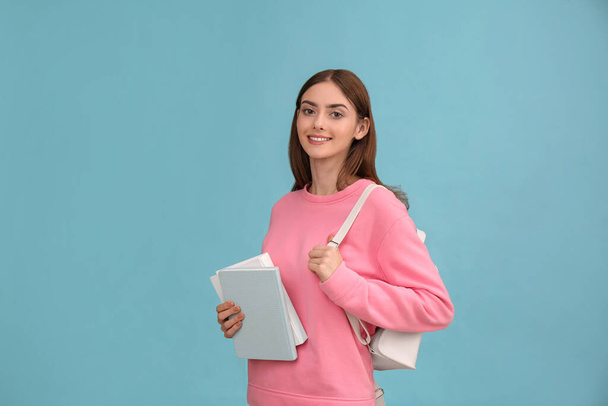 Teenage student with books and backpack on turquoise background - Foto, afbeelding