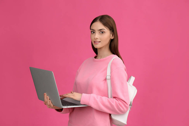 Teenage student with laptop and backpack on pink background - Foto, afbeelding
