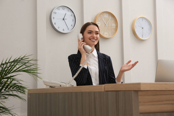 Beautiful receptionist talking on phone at counter in hotel - Foto, Imagem