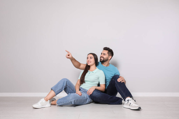 Young couple sitting on floor near light grey wall indoors - Foto, immagini