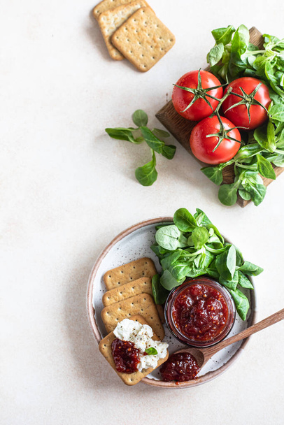 Tomato jam, confiture or sauce in glass jar with crackers and green leaves salad. Unusual savory jam. Mediterranean cuisine. Top view. - Foto, afbeelding