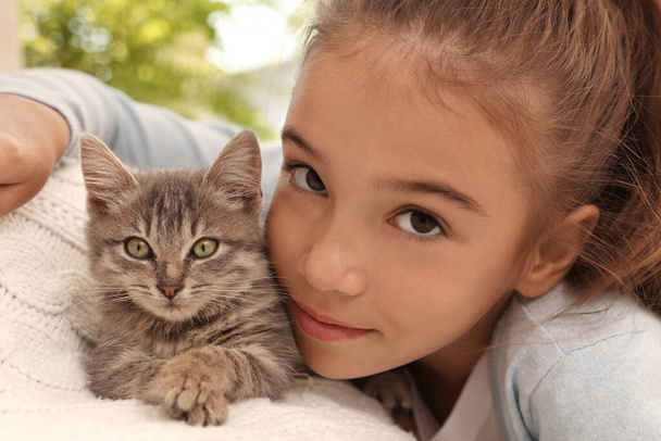 Cute little girl with kitten on white blanket at home, closeup. Childhood pet - Foto, Imagen