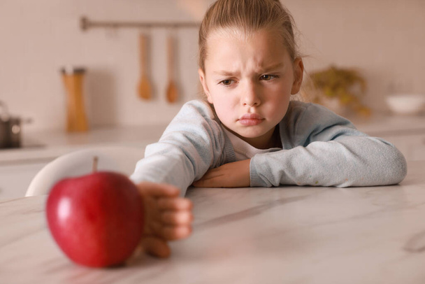 Cute little girl refusing to eat apple in kitchen - Foto, imagen