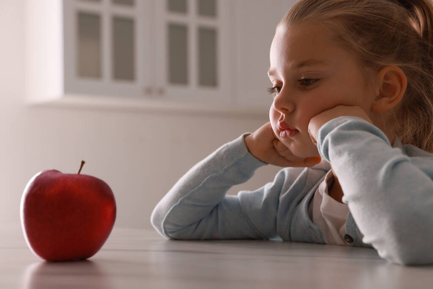 Cute little girl refusing to eat apple in kitchen - Фото, зображення