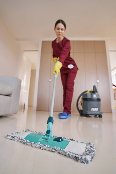 Dark-haired woman in rubber gloves mopping living room - Foto, immagini