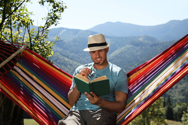 Handsome man reading book in hammock outdoors on sunny day - Фото, зображення