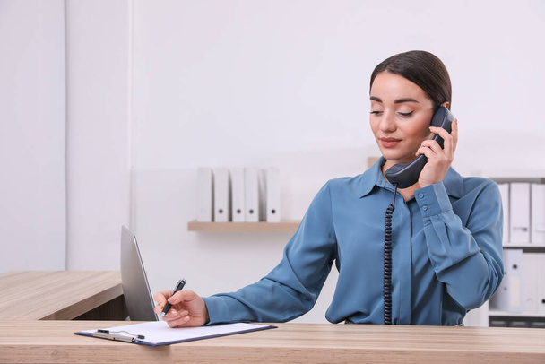 Female receptionist with clipboard talking on phone at workplace - Φωτογραφία, εικόνα