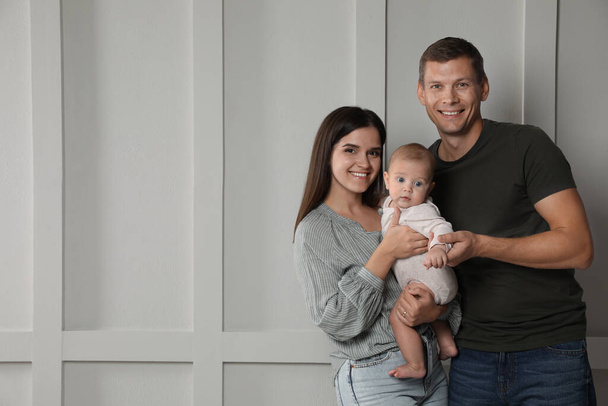 Glückliche Familie. Paar mit süßem Baby in der Nähe einer Lichtwand, Platz für Text - Foto, Bild