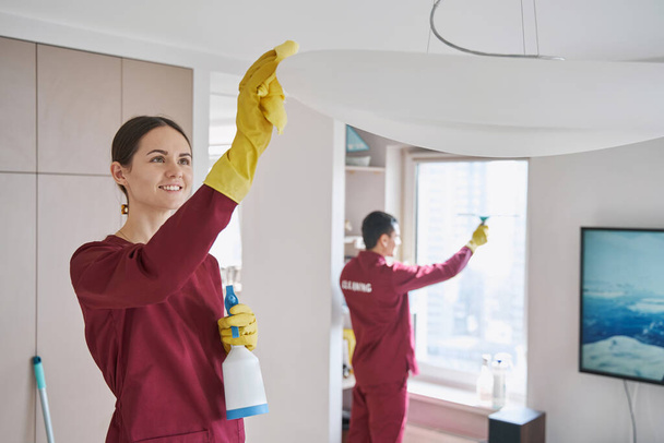 Joyous female cleaner and her colleague cleaning living room - Photo, image