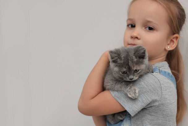 Cute little girl with kitten on light background, space for text. Childhood pet - Photo, Image