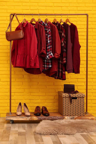 Stojan se stylovým oblečením a taškou v blízkosti žluté cihlové zdi vnitřní - Fotografie, Obrázek