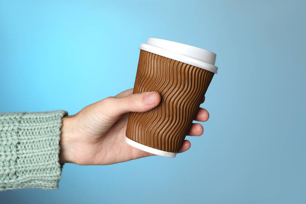 Woman holding takeaway paper coffee cup on blue background, closeup - 写真・画像