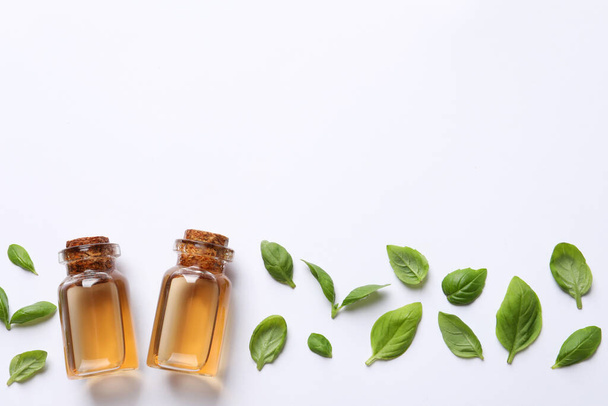 Bottles of essential basil oil and fresh leaves on white background, flat lay. Space for text - Foto, imagen