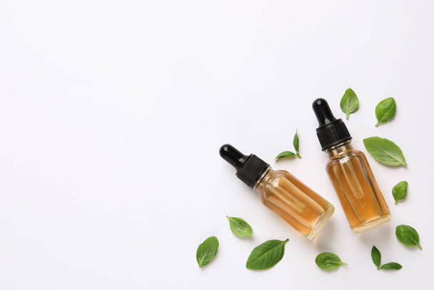Bottles of essential basil oil and fresh leaves on white background, flat lay. Space for text - Fotó, kép