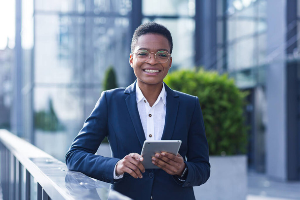 Successful business woman smiling and happy enjoys tablet computer during break, african american woman at office outside - Fotoğraf, Görsel