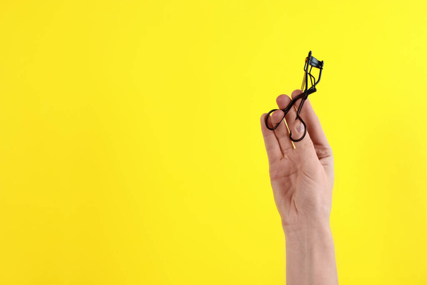 Woman holding eyelash curler on yellow background, closeup. Space for text - Fotografie, Obrázek