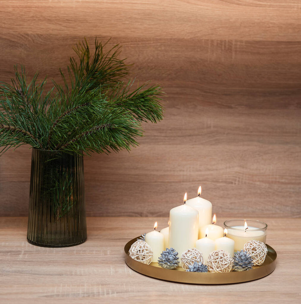 Vánoční výzdoba. Borovicové větve ve ve váze a svíčky na podnose na stole - Fotografie, Obrázek