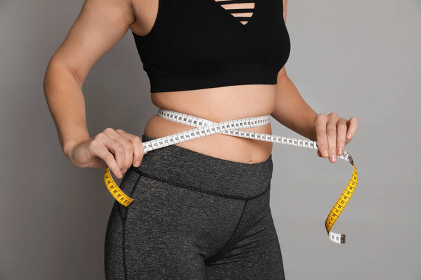 Woman measuring waist with tape on grey background, closeup - Zdjęcie, obraz