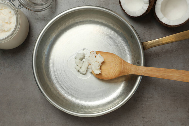 Frying pan with coconut oil and wooden spatula on grey table, flat lay. Healthy cooking - 写真・画像