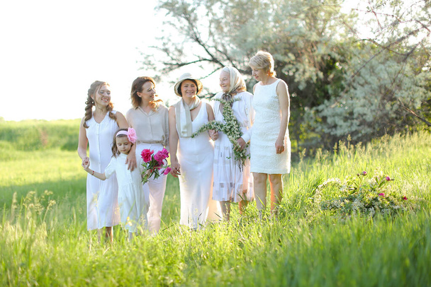 Lächelnde Oma umarmt Töchter und Enkelinnen, trägt weiße Kleidung draußen. - Foto, Bild