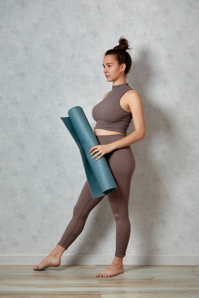 Улыбающаяся беременная женщина в спортивной одежде готова к утренней гимнастике или упражнениям. Счастливая молодая женщина следовать здоровому образу жизни во время беременности, провести коврик для йоги для пилатеса или растяжения - Фото, изображение
