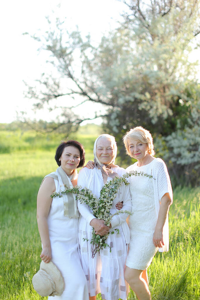Портрет счастливой бабушки с двумя дочерьми под открытым небом в белом платье. - Фото, изображение
