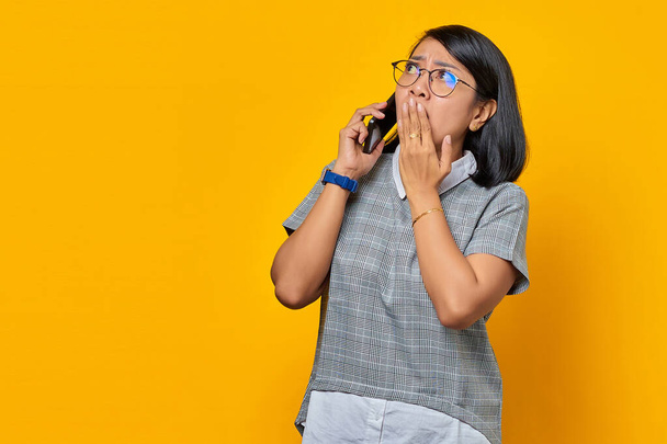 Surpris jeune femme asiatique sur la réception d'un appel entrant sur téléphone mobile et couvrant la bouche avec la main - Photo, image