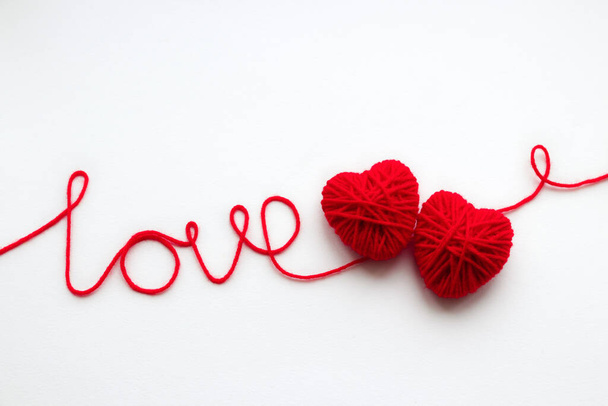 Red inscription "love" and two hearts made of yarn on a white background - Foto, Bild
