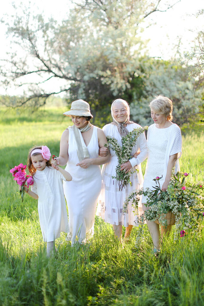 Amerikaanse grootmoeder in witte jurk met dochters en kleindochter buiten. - Foto, afbeelding