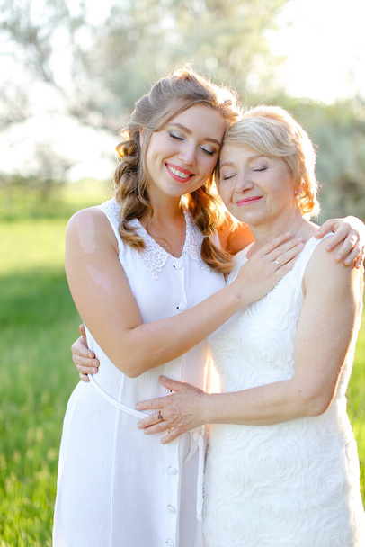 Ritratto di ragazza che abbraccia la madre fuori e indossa un vestito bianco. - Foto, immagini