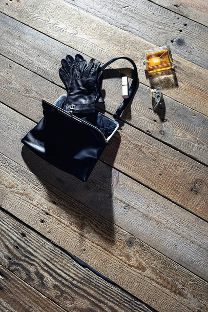 Dames schoonheid accessoires gemorst uit een zwarte leren handtas gevallen op een houten vloer. - Foto, afbeelding