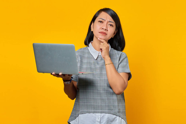 Porträt einer selbstbewussten Asiatin mit Laptop und Blick in die Kamera vor gelbem Hintergrund - Foto, Bild