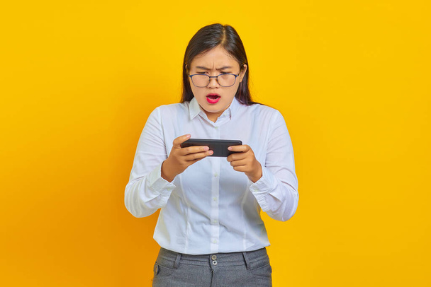 Schockiertes Foto von Geschäftsfrau beim Online-Spiel auf Handy auf gelbem Hintergrund - Foto, Bild