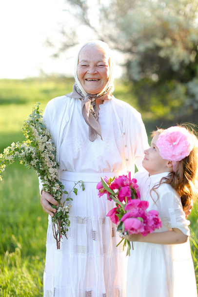 Vanha onnellinen isoäiti seisoo pienen lapsenlapsen kanssa ja pitää kukkia. - Valokuva, kuva