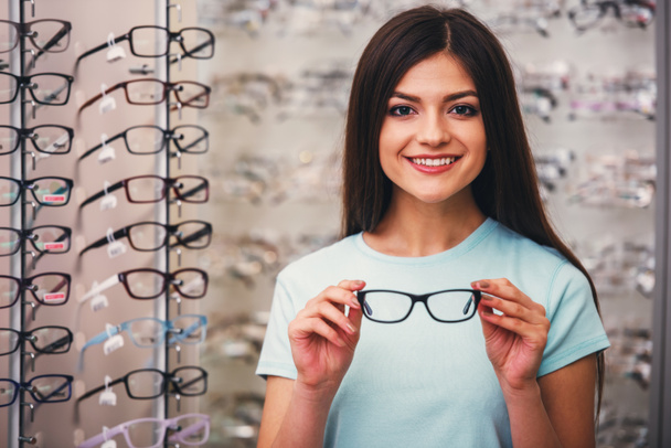 Young woman is choosing a glasses in optician store. - Photo, Image