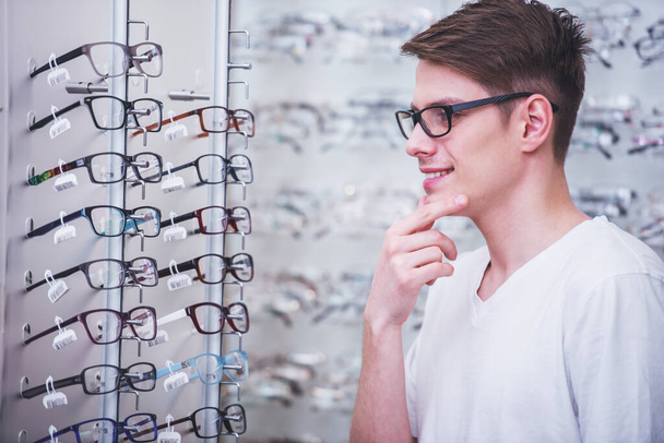 Vue latérale du jeune homme choisit des lunettes dans le magasin
. - Photo, image