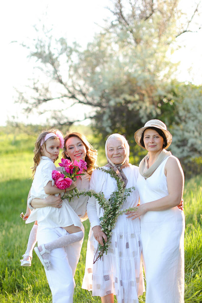 Caucasian grandmother in white dress with daughter and granddaughters outdoors. - Photo, Image