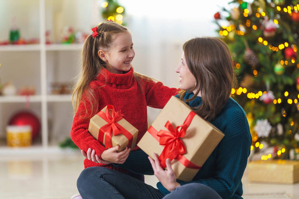 Merry Christmas and Happy Holidays Happy mom and daughter hugging, and hold with christmas gift box on background Christmas tree decorated with a garland. Copy space - Fotografie, Obrázek