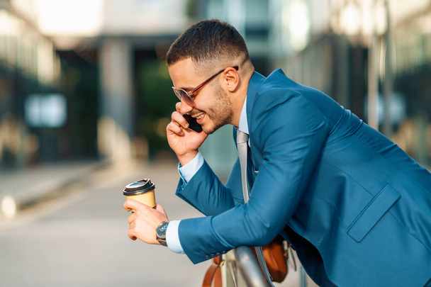 Бизнесмен держит умный телефон. Привлекательный молодой бизнесмен пользуется мобильным телефоном на открытом воздухе. - Фото, изображение