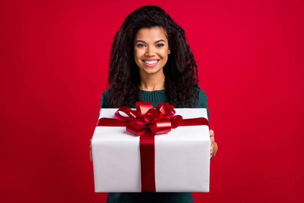 Photo of lucky excited dark skin woman dressed green pullover smiling holding big gift isolated red color background - Foto, immagini