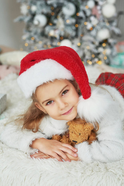 Χριστουγεννιάτικο παιδί στο καπέλο santa στο φόντο του χριστουγεννιάτικου δέντρου. - Φωτογραφία, εικόνα