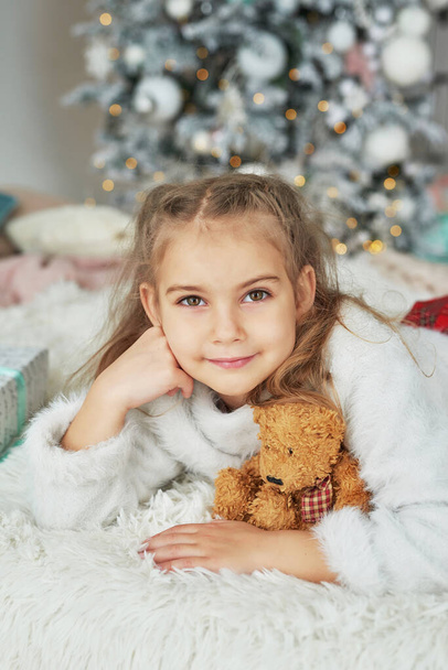 Christmas child on background of Christmas tree with toy teddy bear - Photo, Image