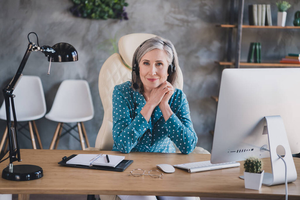 Portrait of attractive elderly cheerful woman helpdesk manager talking to client at office work station place indoor - Foto, imagen