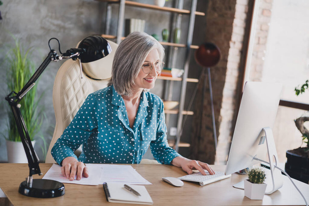 Photo of happy charming old woman business lady look computer smile remote work in office workplace indoors - 写真・画像