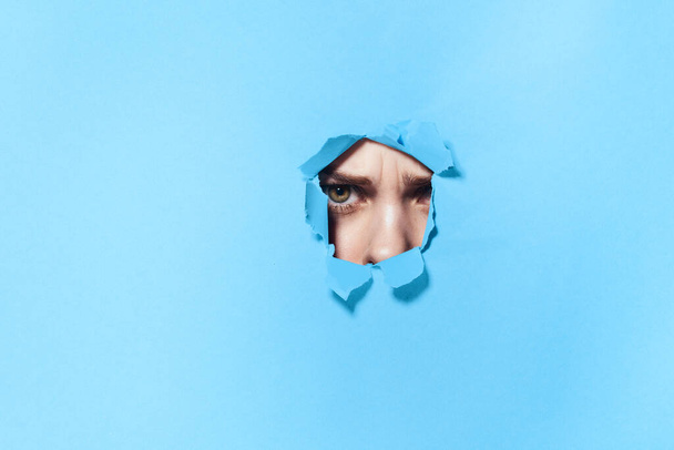 woman peeping through the holes in the poster blue studio background - Фото, зображення