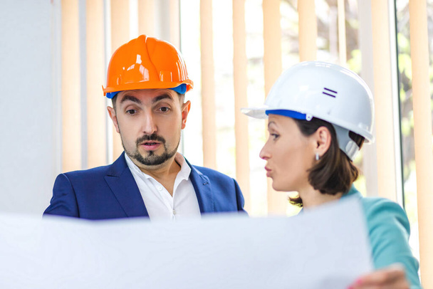 Photo of two engineers wearing helmets and holding paper with plan. - Foto, immagini
