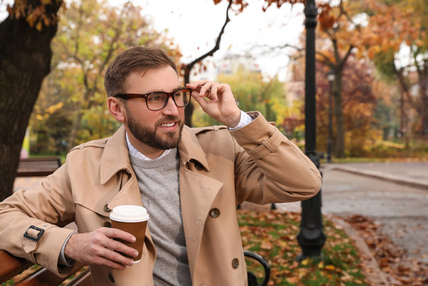 Handsome man wearing stylish clothes with cup of coffee in autumn park - Photo, image
