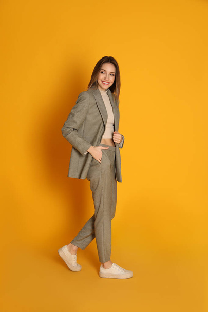 Full length portrait of beautiful young woman in fashionable suit on yellow background. Business attire - Fotografie, Obrázek