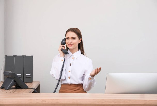 Female receptionist talking on phone at workplace - Фото, зображення