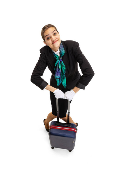 Высокоугольный вид красивой молодой девушки, бортпроводник в форме с чемоданом на белом студийном фоне. - Фото, изображение